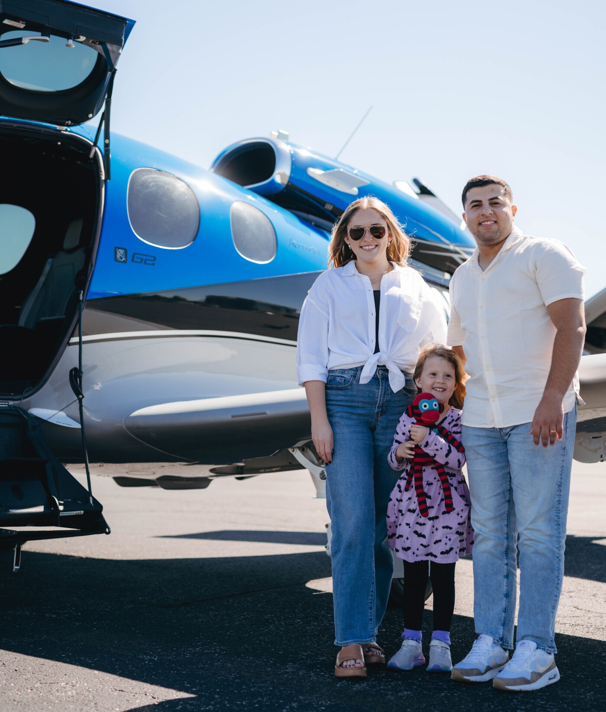 Harmony Air Charter easy Family of three posing beside the Harmony Air Vision Jet on a sunny tarmac, with the door open.
